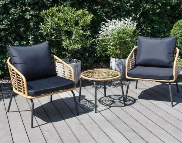 Garden chairs with black cushions and a table on a deck in a garden.