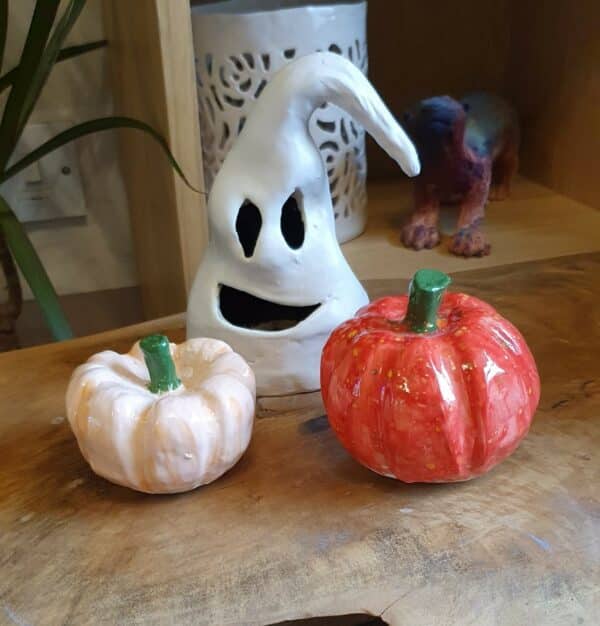 A ghost faced lantern made from clay and two clay pumpkins, one painted white and one orange.