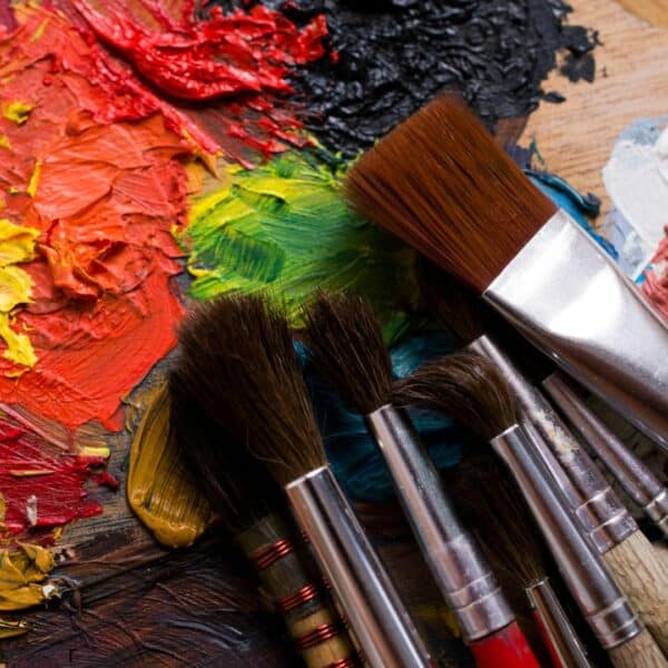 Various sizes of paint brushes laying on a used paint palette.