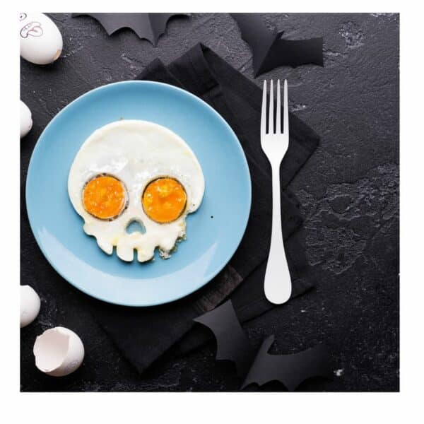 Fried eggs in the shape of a skull on a blue plate with a silver fork on a black background.